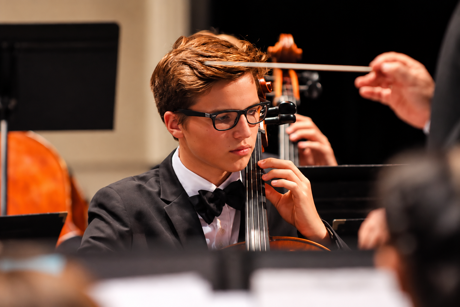 Youth orchestra students performing on stage during concert, emotional moment, black and white photography with dramatic stage lighting